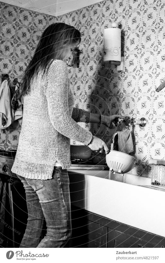 Schöne Frau in Pullover und Jeans steht in einer einfachen Küche