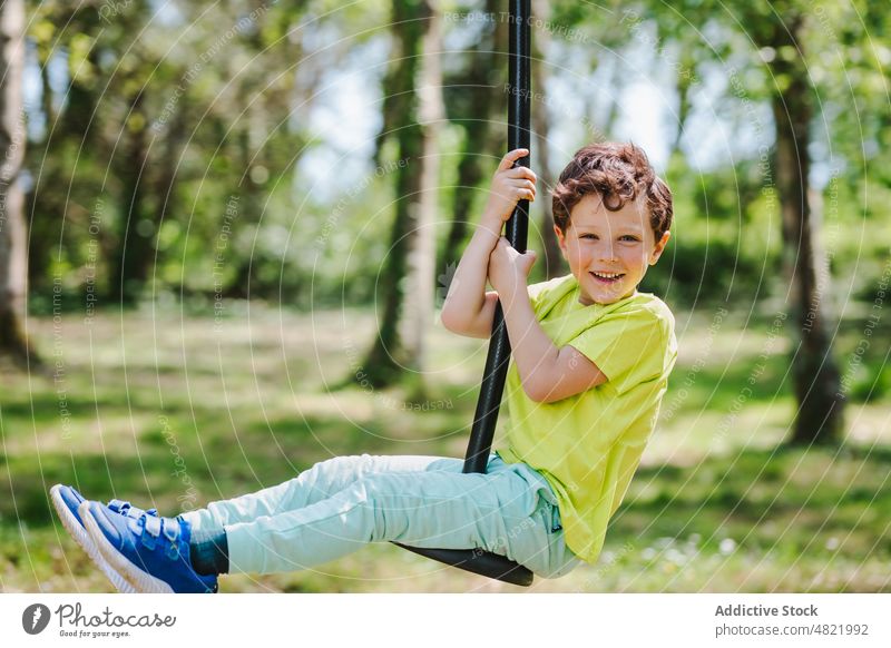 Fröhliches kleines Kind auf dem Schaukelseil auf dem Spielplatz lächelt in die Kamera pendeln Seil Lächeln Kindheit heiter Aktivität Junge Park positiv Porträt