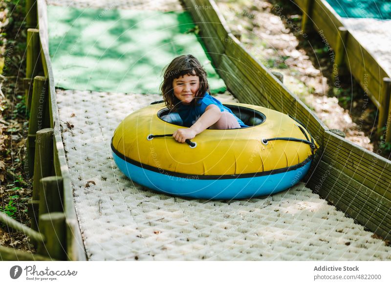 Glückliches kleines Mädchen, das auf einem aufblasbaren Schlitten auf einer Rampe im Park fährt Kind Mitfahrgelegenheit Sliden Tube Aktivität Spielplatz heiter