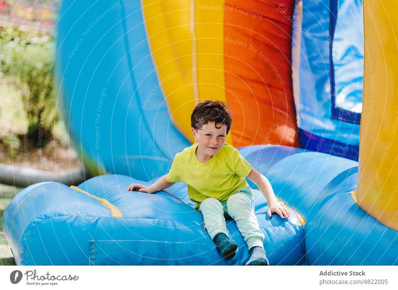 Freudiger kleiner Junge sitzt auf aufblasbarem Trampolin und lächelt Lächeln Spielplatz Burg oder Schloss positiv Freude Kind Vergnügen Porträt Park Kindheit