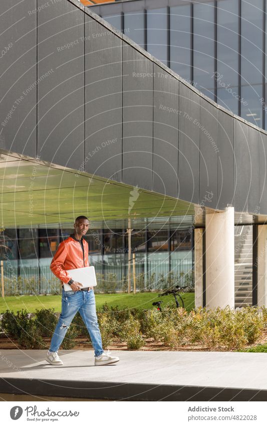 Afroamerikanischer Mann mit Laptop geht nach einem Arbeitstag im Park spazieren Spaziergang Campus Schüler freiberuflich Universität Weg abgelegen selbstbewusst