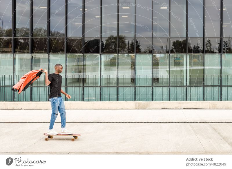 Cooler junger schwarzer Mann fährt Skateboard auf einer modernen Stadtstraße Mitfahrgelegenheit Straße Gebäude trendy Großstadt cool Skater Aktivität Stil