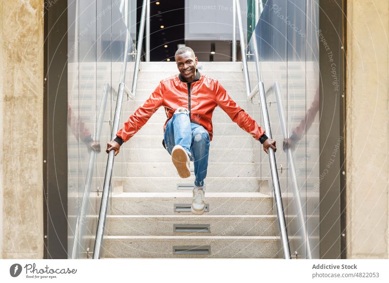 Positiver trendiger schwarzer Typ, der auf der Straße auf eine Treppe springt Mann springen Treppenhaus Lächeln positiv trendy Glück aktiv Trick Reling