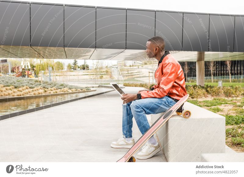 Junger Schwarzer mit Netbook auf einer Bank im Park Mann Arbeit Laptop freiberuflich abgelegen Tippen Konzentration Longboard beschäftigt Großstadt männlich