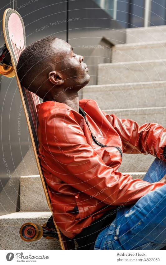Ruhiger afroamerikanischer Mann lehnt sich auf Skateboard auf Straßentreppe Augen geschlossen sich[Akk] entspannen Treppenhaus trendy cool Skater Freizeit ruhen