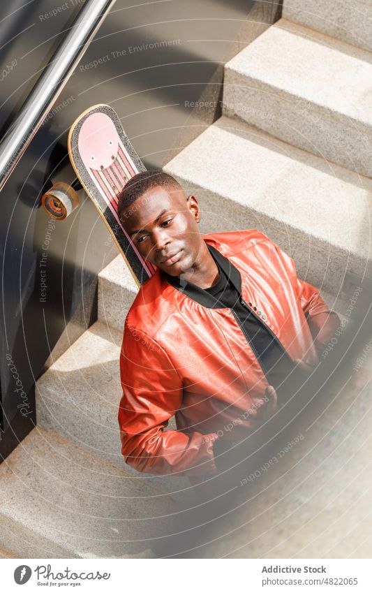 Ruhiger afroamerikanischer Mann lehnt sich auf Skateboard auf Straßentreppe sich[Akk] entspannen Treppenhaus trendy cool Skater Freizeit ruhen Schüler Wegsehen