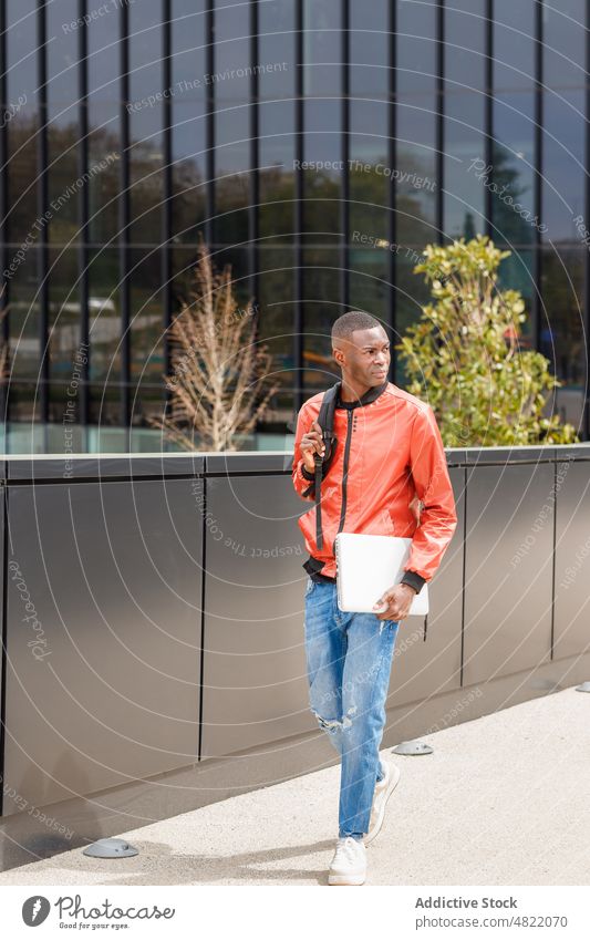 Selbstbewusster schwarzer männlicher Student, der in der Nähe eines modernen Gebäudes in der Stadt spazieren geht Mann Schüler Spaziergang Straße Großstadt