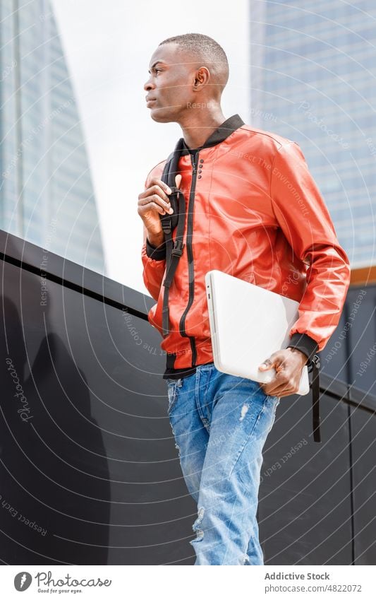 Selbstbewusster schwarzer männlicher Student, der in der Nähe eines modernen Gebäudes in der Stadt spazieren geht Mann Schüler Spaziergang Straße Großstadt