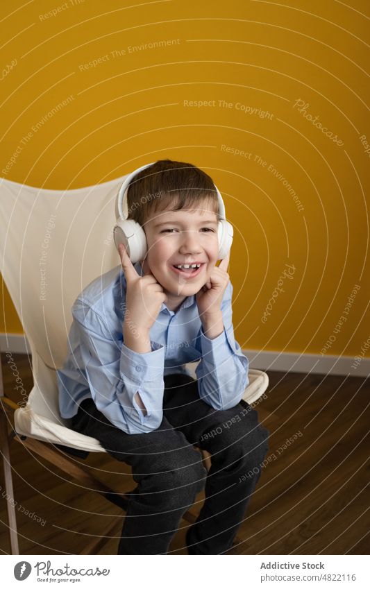 Junge hört auf einem Liegestuhl Musik zuhören heimwärts Lächeln Glück meloman unterhalten Kind smart lässig sitzen Stuhl gestikulieren heiter Kopfhörer Drahtlos