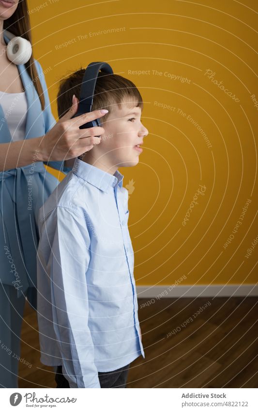 Mutter setzt ihrem Sohn Kopfhörer auf ausrichten Musik zuhören angezogen Zusammensein heimwärts Frau Junge meloman Drahtlos Kind Melodie Eltern Lächeln Liebe