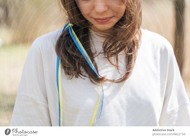 Lächelnde Dame mit blauen und gelben Bändern im Haar in der Natur stehend Frau Ukrainer Fahne Bändchen Windstille Patriotin Porträt feminin Feld Sonnenlicht