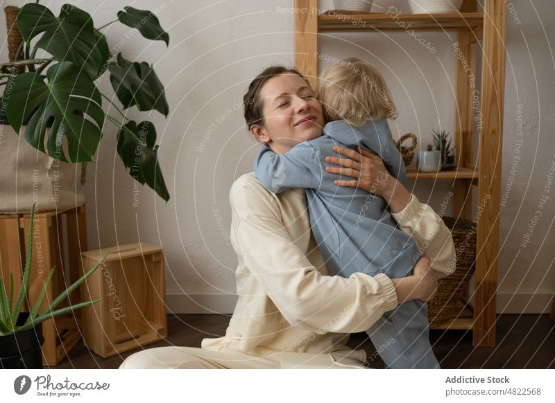 Zufriedene Mutter, die auf dem Boden sitzt und ihr Kind zu Hause umarmt Frau Umarmen Liebe Beine gekreuzt Glück Mutterschaft positiv Appartement