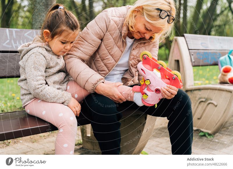 Lächelnde Großmutter, die Rollschuhe an die Füße eines kleinen Mädchens im Park stellt Frau Kind Rollerskate angezogen positiv Hilfsbereitschaft Enkelin