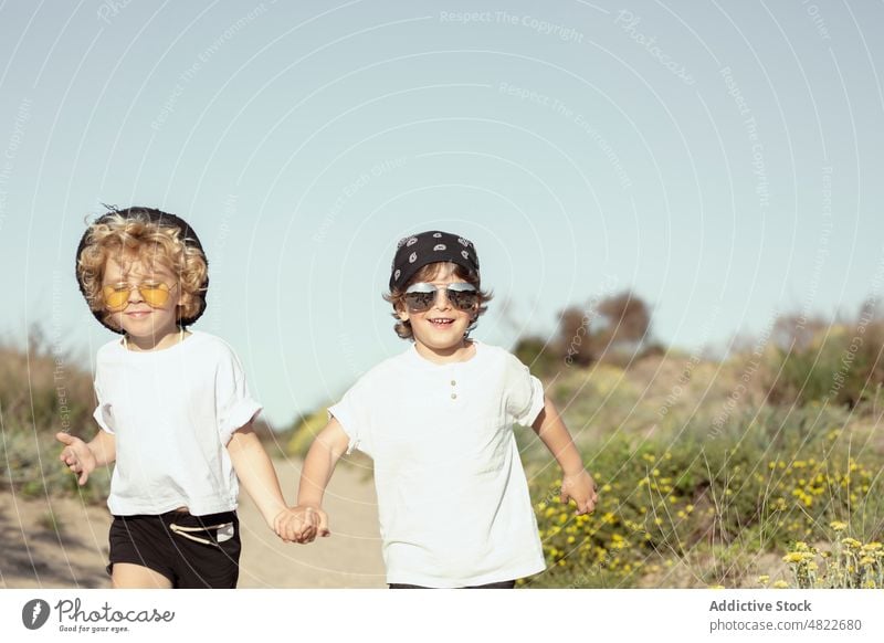 Glückliche kleine Geschwister, die sich beim Spazierengehen am Strand an den Händen halten Kinder Händchenhalten Spaziergang Weg Zusammensein trendy Bruder