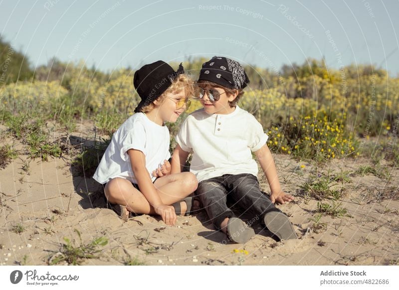 Liebenswerte positive Kinder spielen mit Sand am Strand Feiertag heiter Zusammensein Rücken an Rücken Lächeln Urlaub Bruder Freude Freundschaft Glück trendy