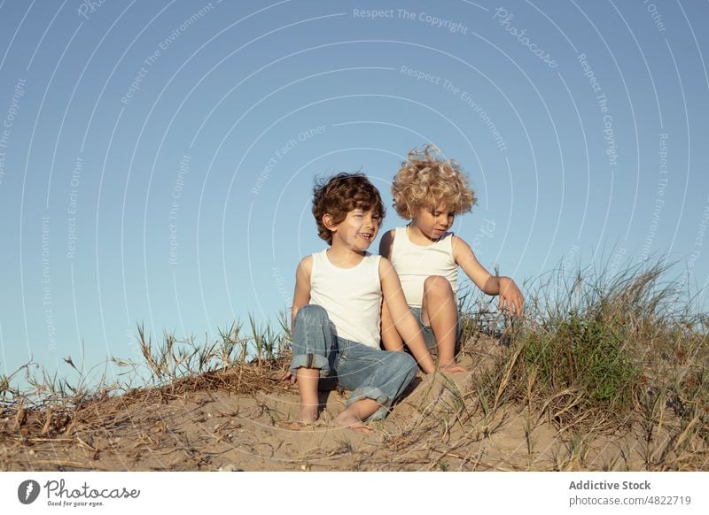 Liebenswerte positive Kinder spielen mit Sand am Strand Feiertag heiter Zusammensein Lächeln Urlaub Bruder Freude Freundschaft Glück trendy blond Stil Küste