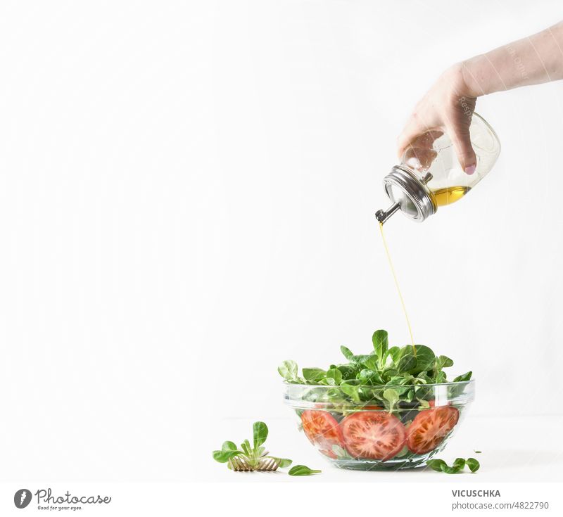Frau Hand gießt Öl über große Schüssel mit Salat. Gesundes Essen. Gießen Erdöl Schalen & Schüsseln Salatbeilage Herstellung frisch grün Tomaten Olivenöl