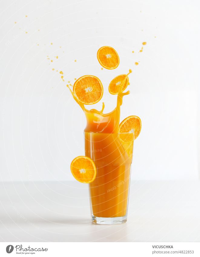 Glas mit Spritzern von Orangensaft und fallenden Orangenscheiben auf weißem Hintergrund Geplätscher Orangenscheibchen Tisch weißer Hintergrund Gesundheit