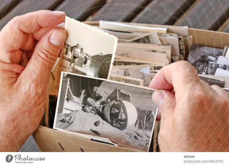 zwei Hände eines Mannes halten alte Schwarzweißfotos vom Strandurlaub zum Betrachten / Urlaubserinnerung / analoge Fotografie Urlaubsbilder Papierbild