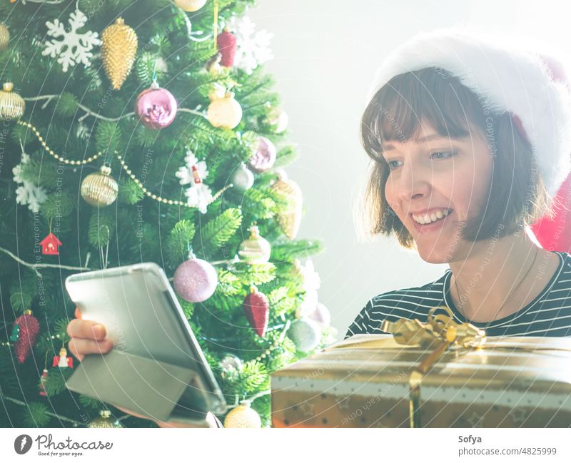 Lächelnde Frau hält eingepackte Geschenke mit Tablet in der Nähe von Weihnachtsbaum Weihnachten Tablette Glück kaufen online benutzend gestapelt heimwärts
