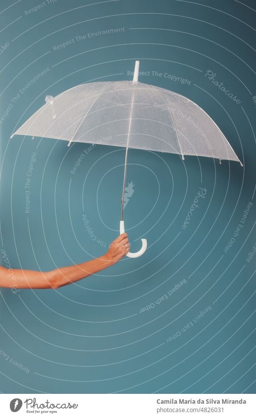 Weibliche Hand hält einen transparenten Regenschirm auf blauem Hintergrund. Foto im Studio. Accessoire Herbst Klima fallen Mode Frau frisch Beteiligung liquide