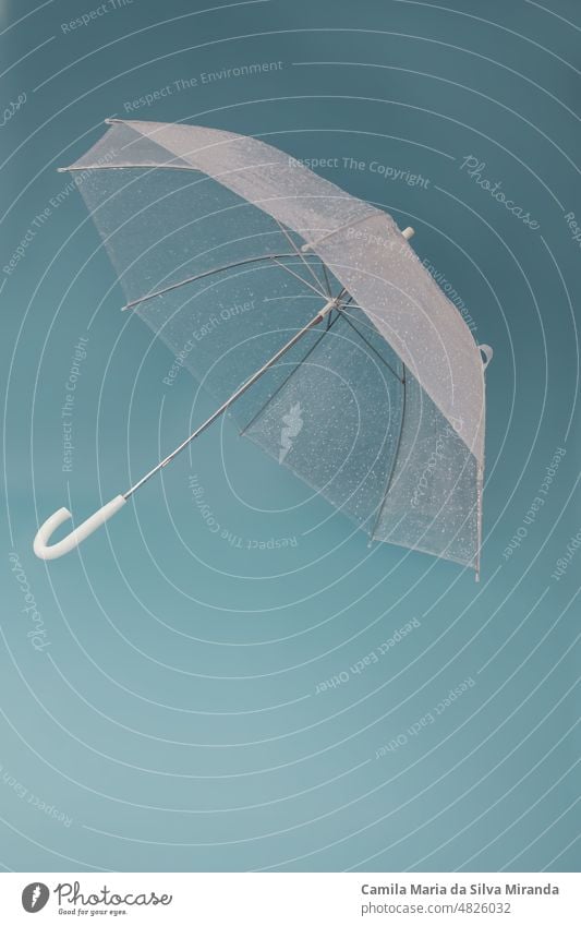 Transparenter Regenschirm auf blauem Hintergrund. Foto im Studio. Accessoire Herbst Klima Konzept fallen Mode frisch Hand liquide Schutz Regentropfen regnerisch