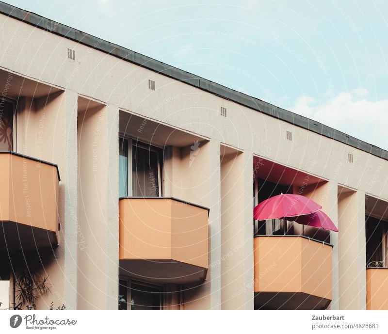Mehrfamilienhaus mit wabenförmigen Balkons in beige sowie rosa Sonnenschirm Wohnung wohnen hellbraun lachsfarben Schirm Idylle Glück fassade Mietshaus Stadt
