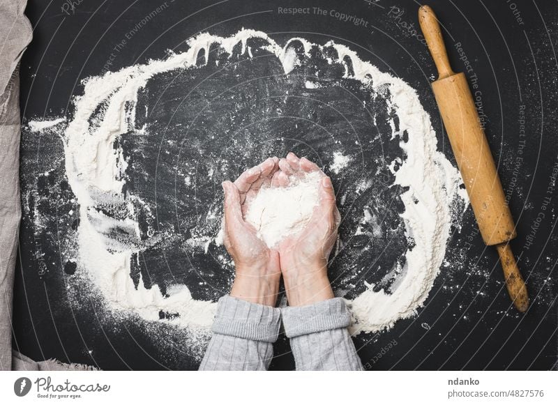 zwei Frauenhände halten eine Handvoll weißes Weizenmehl auf einem schwarzen Tisch, Draufsicht Bäcker Bäckerei backen Brot Koch Essen zubereiten Küche Teigwaren