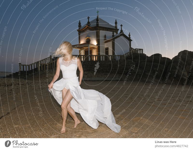 Was für eine romantische Art, an einem Strand in Porto, Portugal, zu heiraten. Eine kleine Kirche steht am Meer, der Himmel ist lila an diesem schönen Abend, und eine wunderschöne blonde Braut trägt ein weißes Hochzeitskleid. Allerdings ist kein Bräutigam auf dem Bild zu sehen.