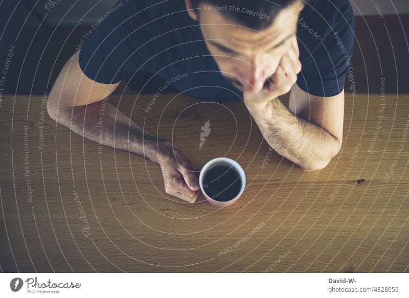 Mann sitzt am Tisch mit einer Tasse Kaffe in der Hand Kaffee sitzen warten gelangweilt genervt Kaffeebecher Kaffeepause nachdenklich Gedanken Sorgen