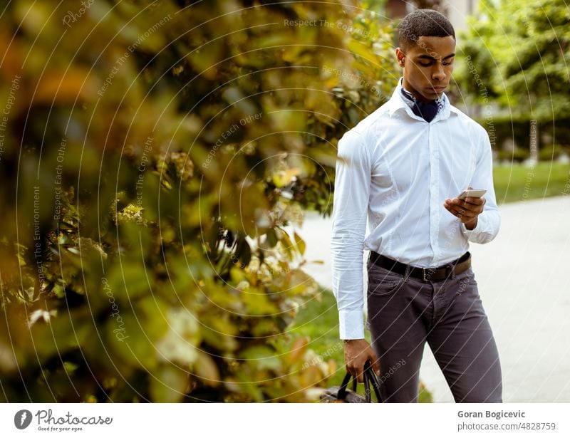 Junger afroamerikanischer Geschäftsmann, der ein Mobiltelefon benutzt, während er auf einer Straße geht Amerikaner schwarz Gebäude Business Anruf Aufruf kausal