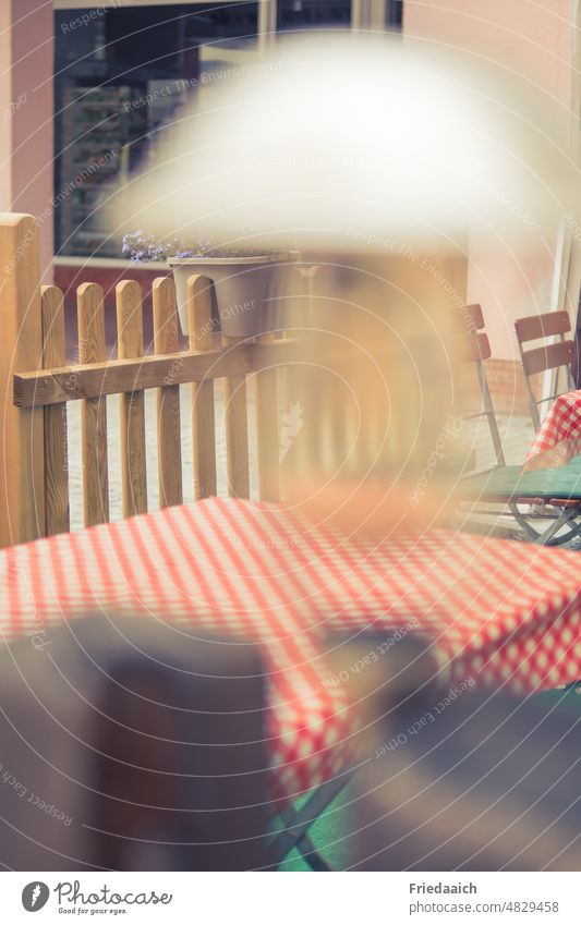 Biergarten-Detailaufnahme mit rot-weiß karierter Tischdecke, Holzzaun im Hintergrund und unscharfer Lampe im Vordergrund r Tischdecken im Freien rotweiß Karo