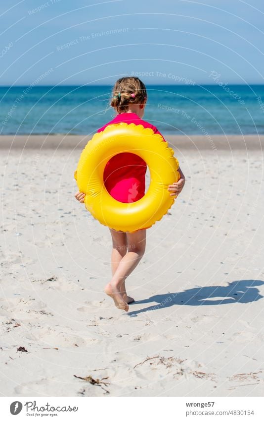 Mädchen läuft am Ostseestrand mit einem gelben Schwimmring auf dem Rücken Richtung Meer Schwimmreifen laufen Sandstrand Rückansicht Küste Strand