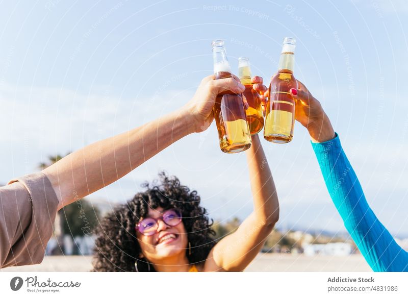 Unterschiedliche Freunde stoßen am Strand an Zuprosten Bier Picknick Sommer Zusammensein Lächeln Klirren Flasche Mann Frauen vielfältig rassenübergreifend