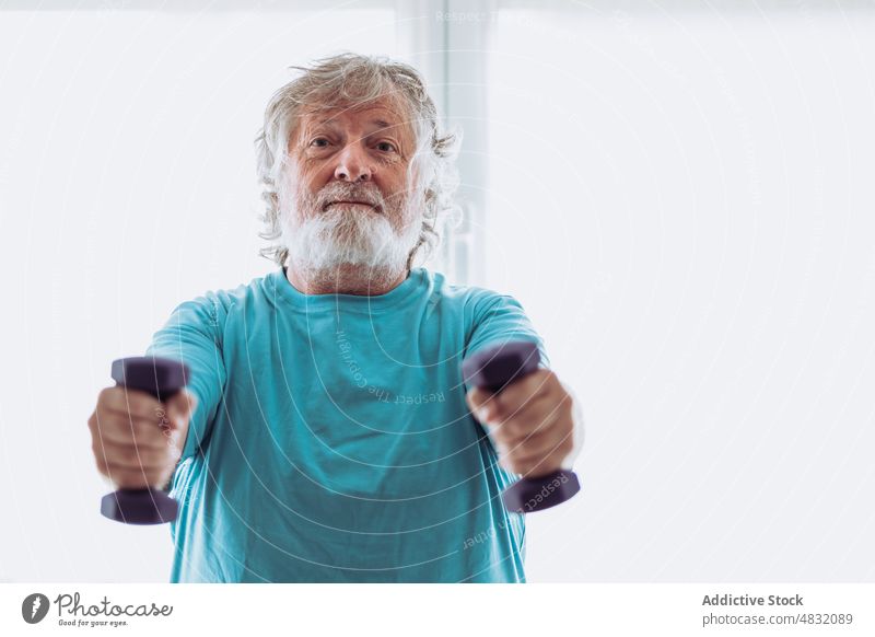 Fröhlicher älterer Mann beim Training mit Hanteln Übung Kurzhantel Lächeln Morgen heimwärts Fitness Glück gymnastisch männlich Senior gealtert Rentnerin