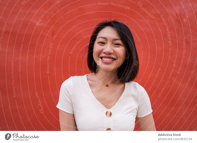 Erfreute junge ethnische Frau lächelt in die Kamera vor einer roten Wand Lächeln heiter selbstsicher Persönlichkeit positiv Porträt Glück charismatisch froh