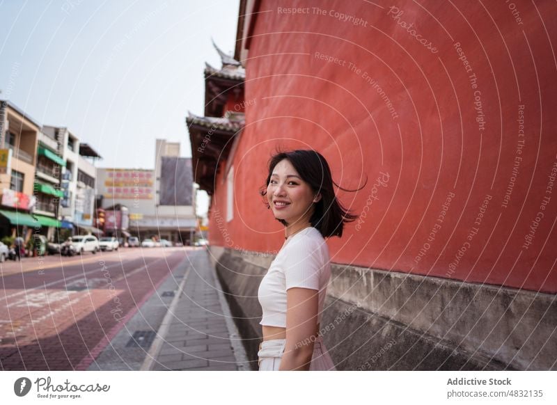 Junge ethnische Frau lächelt in die Kamera vor einer roten Wand Lächeln heiter selbstsicher Persönlichkeit positiv Porträt Glück charismatisch froh Optimist