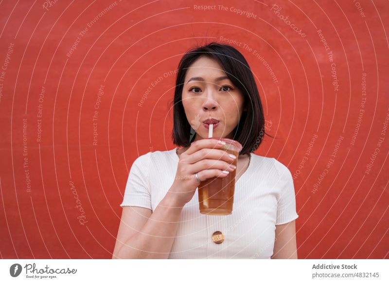 Junge ethnische Frau trinkt ein erfrischendes Getränk zum Mitnehmen auf der Straße trinken Kaffee Erfrischung Imbissbude Porträt selbstbewusst Stil Stroh jung