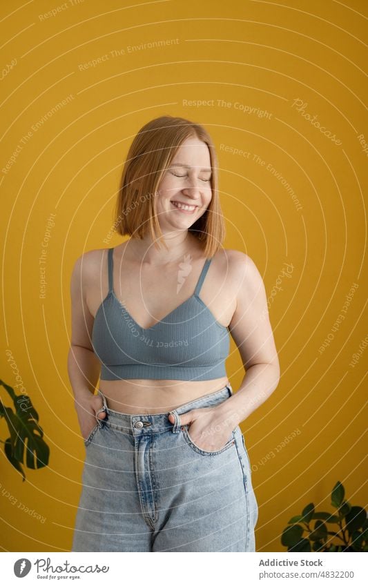 Positiv gestimmte junge Frau im BH, die mit geschlossenen Augen strahlend lächelt Lächeln Augen geschlossen heiter Hand-in-Tasche selbstbewusst Glück Model