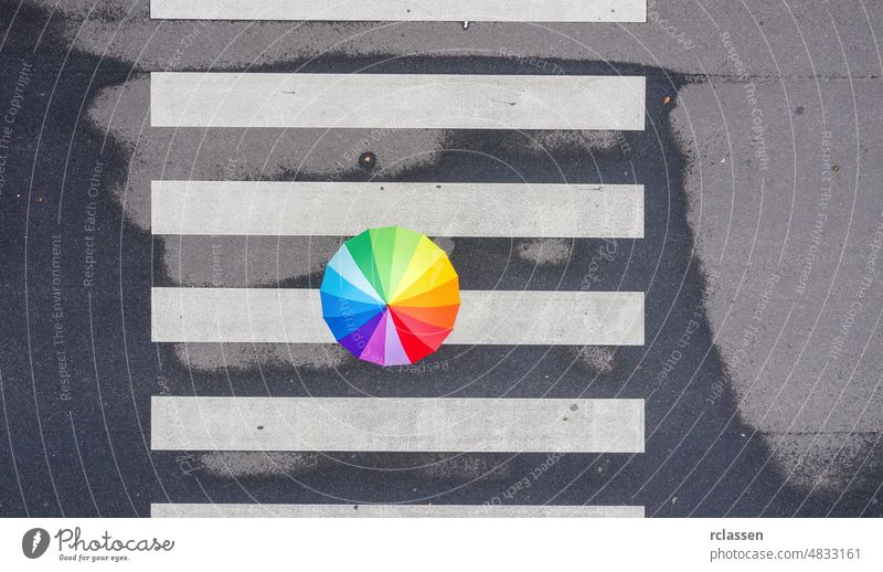 Draufsicht auf einen Regenbogenschirm auf einem Fußgängerüberweg Regenschirm Top Überfahrt Ansicht Farbe Zebrastreifen Dröhnen Straße Großstadt laufen
