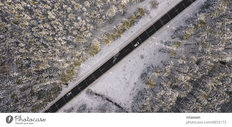 Luftaufnahme eines verschneiten Waldes mit einer Straße und einem Auto. Von oben mit einer Drohne aufgenommen Winter Dröhnen Antenne Sonnenuntergang Sonnenlicht