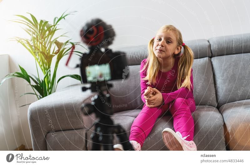 Schönes junges Mädchen in rosa Freizeitkleidung lächelnd in die Kamera und sprechen auf Videoaufnahmen mit Technologie. Kinder Social-Media-Influencer oder junge Content-Maker-Konzept in entspannten lässigen Stil zu Hause.