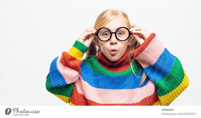 kleines Mädchen ist erstaunt und ihre Hände berühren Brillen tragen Regenbogen-Stil Pullover und hispter Brille isoliert auf weißem Hintergrund Kind verrückt