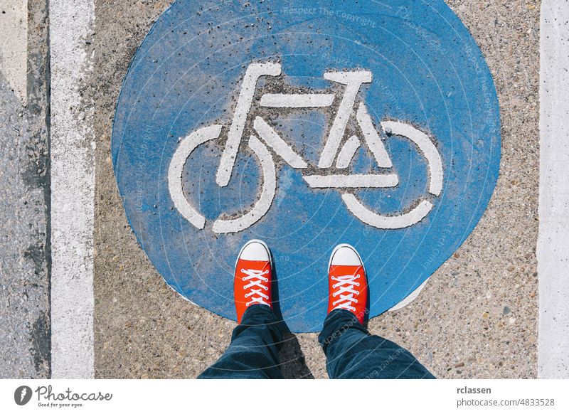 Mann stehend auf Fahrrad-Zone Zeichen auf einer asphaltierten Straße in roten Turnschuhen, Perspektive pov konzeptionell Stock urban Schritt blau Konzept Boden