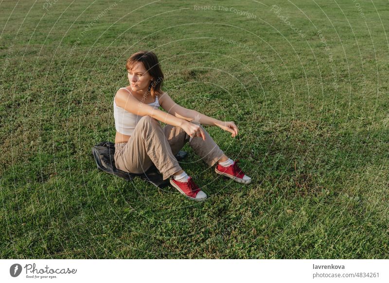 Junges Weibchen, das während der goldenen Stunde im Freien auf einer Wiese sitzt, Frau jung menschlich grün Wellness Gras Sommer allein Natur Porträt Kaukasier