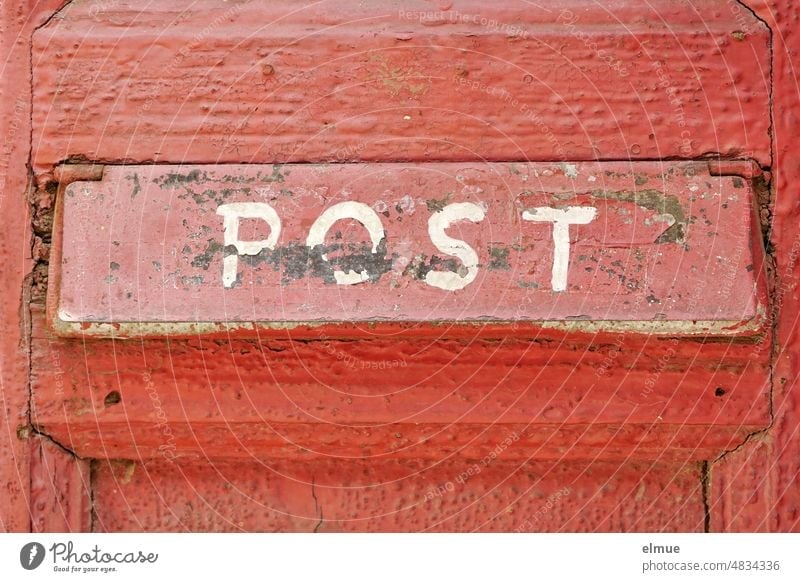 Am roten Posteinwurfschlitz an einer alten rot gestrichenen Holztür steht in weißen Großbuchstaben handgeschrieben POST Tür Türschlitz Zeitungsschlitz