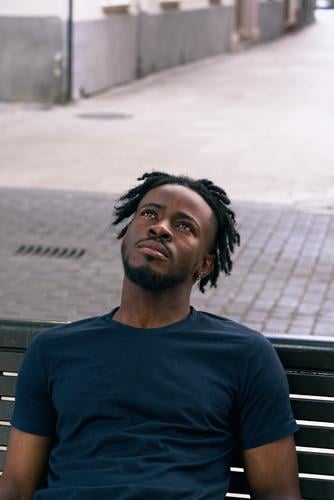 junger farbiger Mann ruht auf einer Bank Gesicht faceup Porträt Alleine Lässig Stadt Draußen Spanien Straße Zwanziger Jahre Trendy Urban Junge Freizeitkleidung