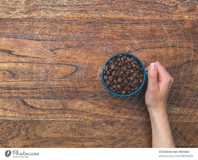 Jetzt einen starken Kaffee ... Kaffeetasse Kaffeebohnen Kaffeebohnen in einer Tasse Tischplatte Holztischplatte Hand Arm heiß rösten Lifestyle Bohnen geröstet