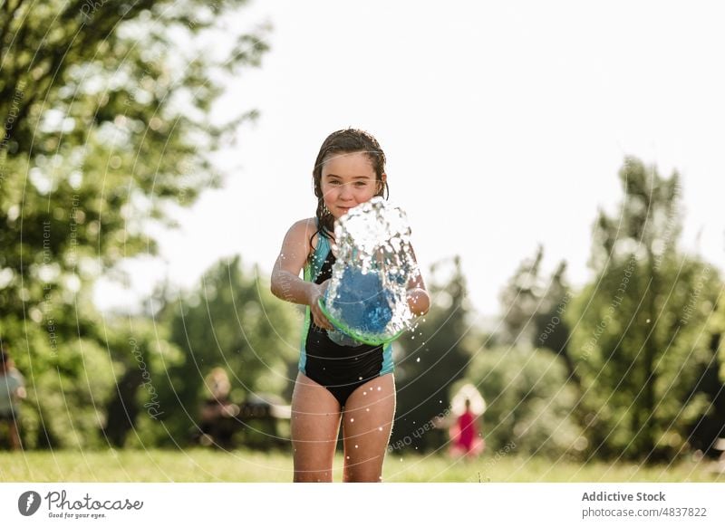 Kleines Mädchen spielt mit Eimer im Park Sommer Frau Werfen Wasser in Richtung Fotokamera selbst Feiertag Kindheit Lifestyle Freude Saison jung genießen Garten