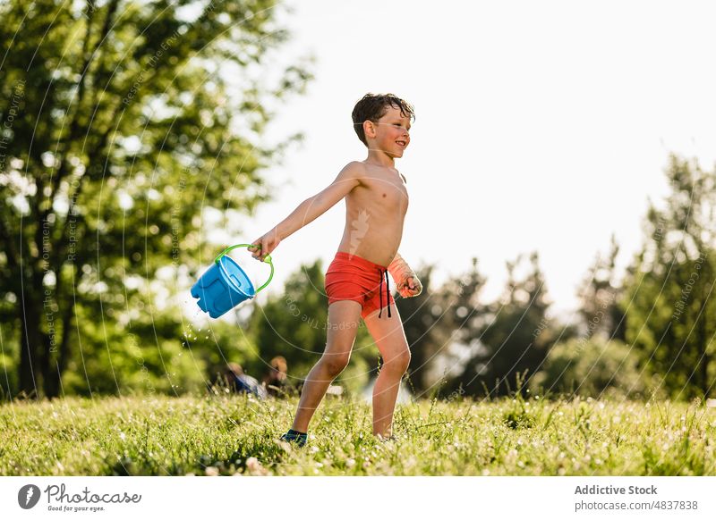 Glücklicher Junge spielt mit Wasser ohne Hemd Kindheit Sommer Park Rasen Natur Aktivität Athlet sorgenfrei nackter Torso wenig heiter Wiese Zusammensein Sonne